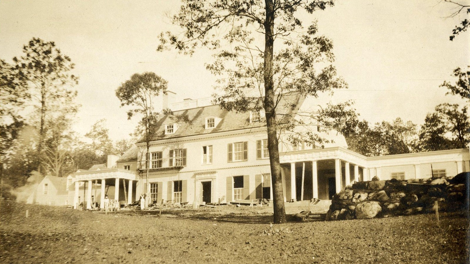 Black and white of large white home with grassy area in front with some trees