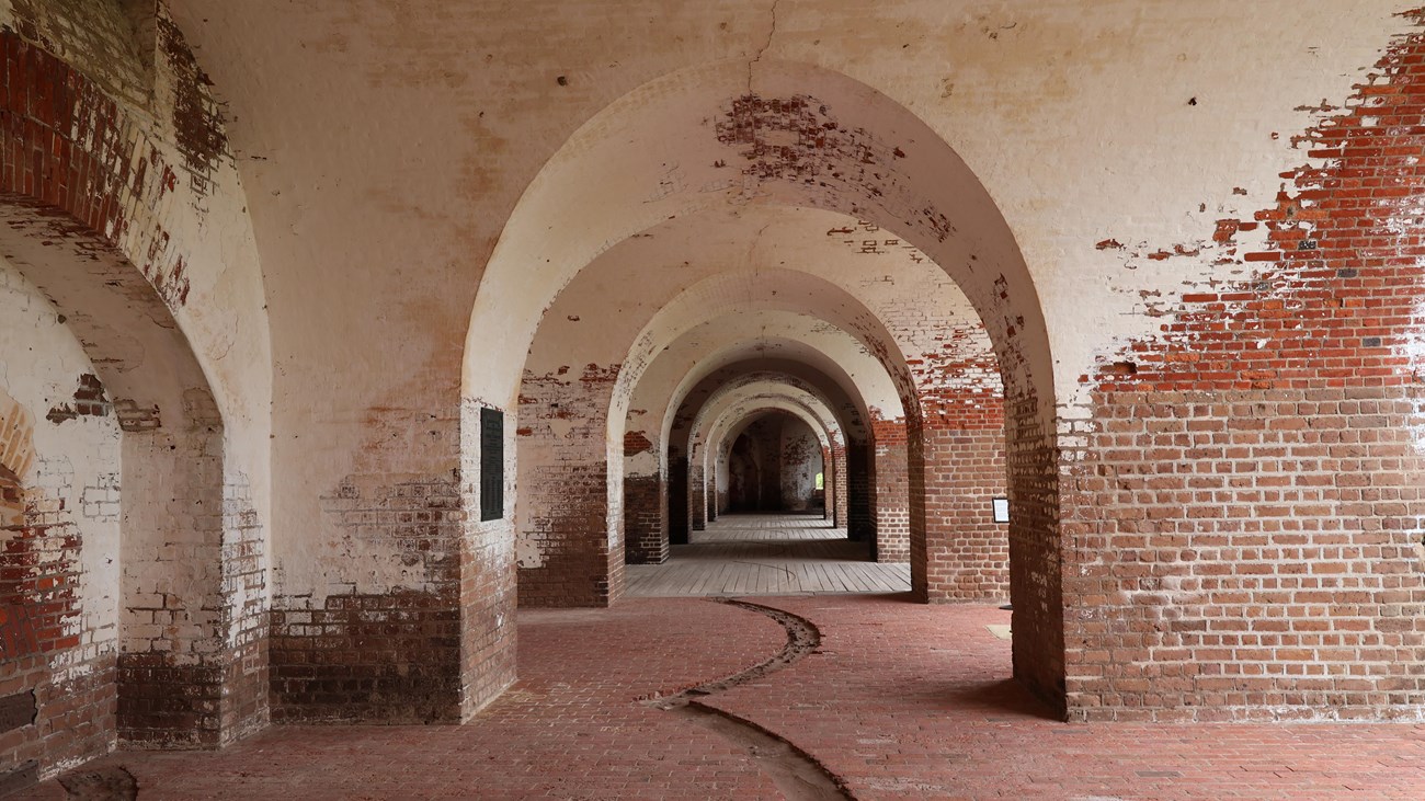 Interior of a brick structure with thick walls, arches separate several rooms. 