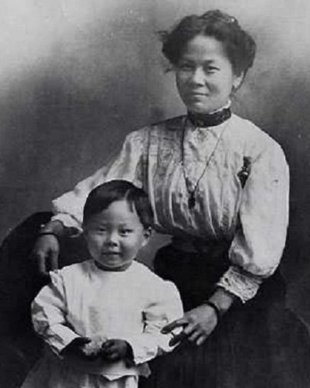 Portrait of Chinese woman wearing long sleeved white blouse and dark skirt with toddler age son