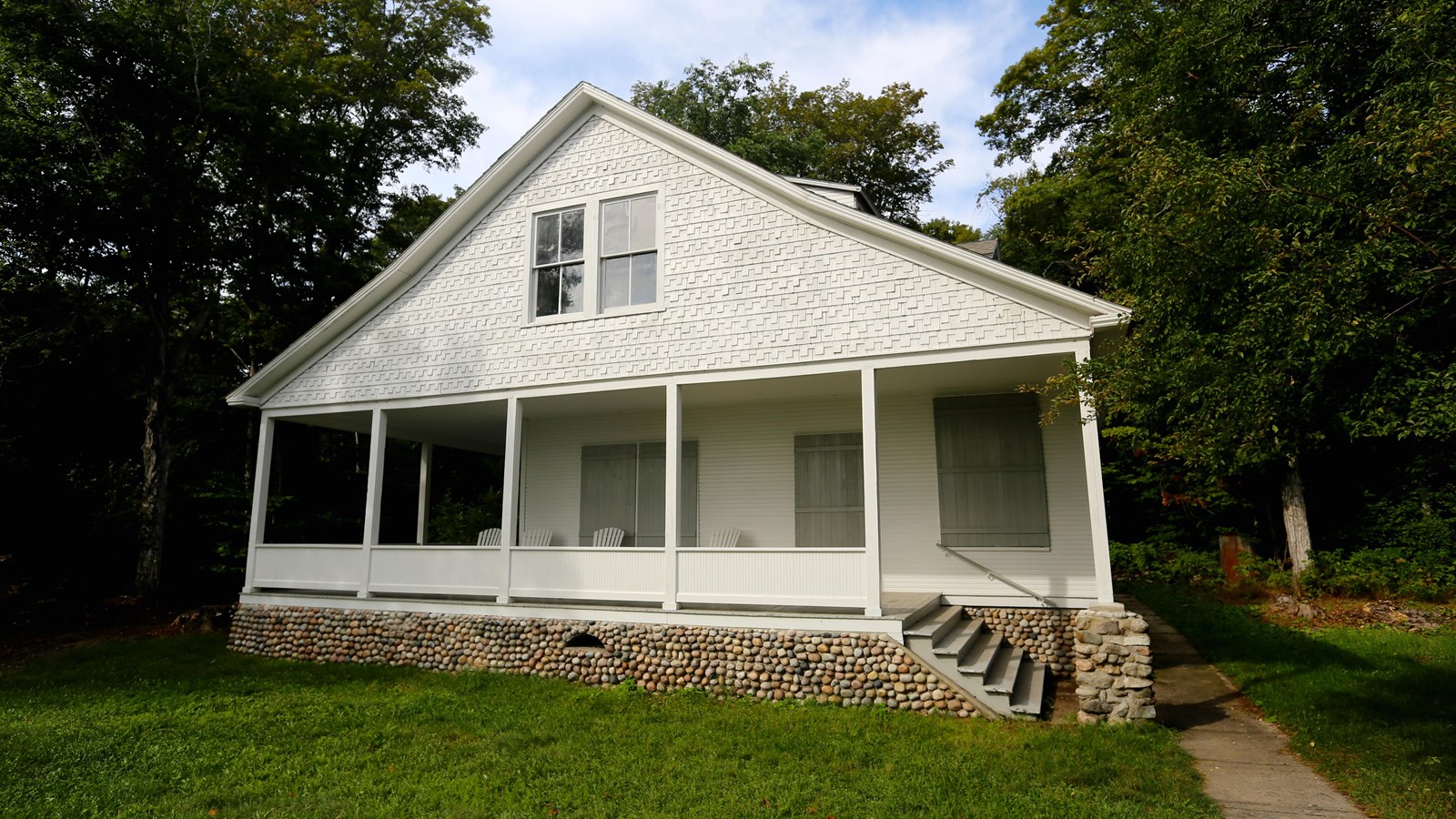 A white, wooden house with an elevated front porch set on a foundation of river stones.