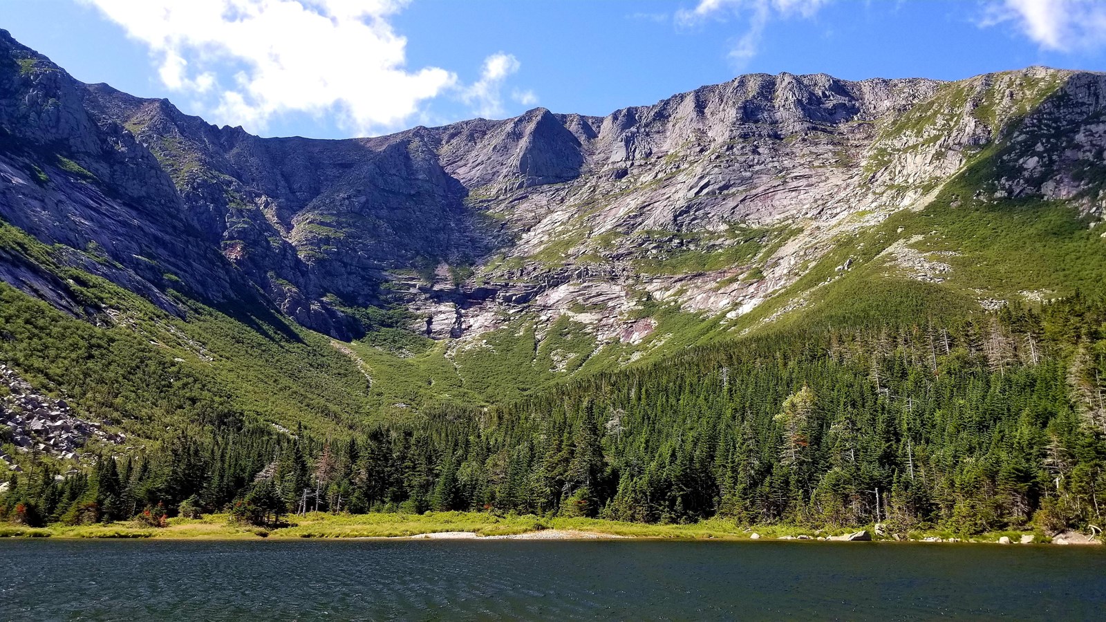 Pond with rising granite mountain above treeline in the background.