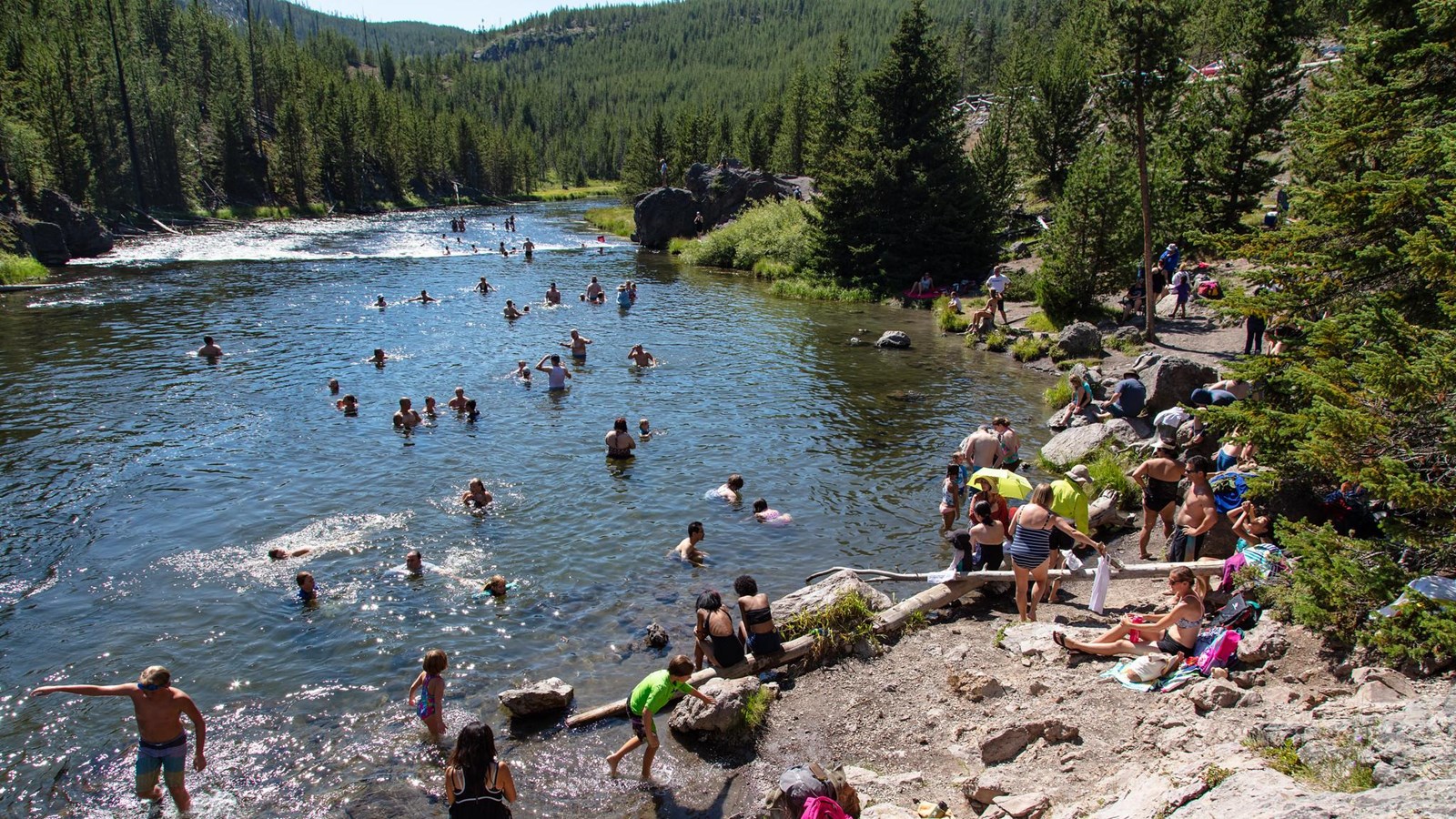 A crowd of people gathers to swim in a river.