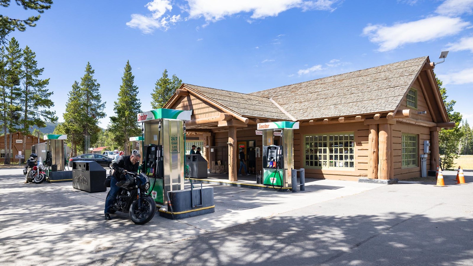 Four gas pump stations in front of a building with covered entrance and wood shingled roof.