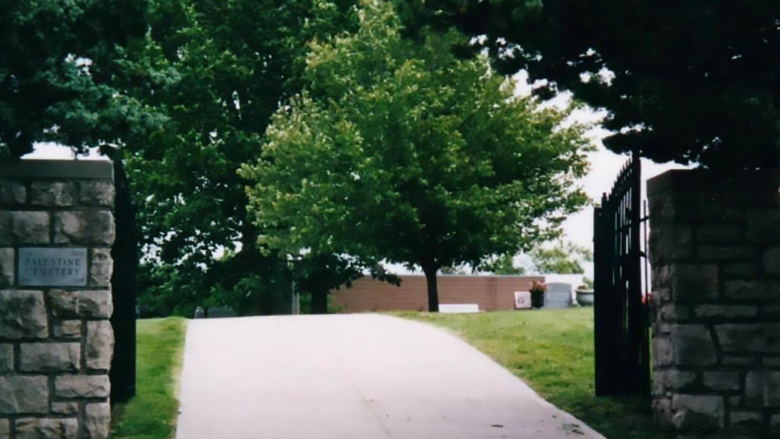 Stone and metal entrance gate to cemetery with pathway leading to grassy space with trees