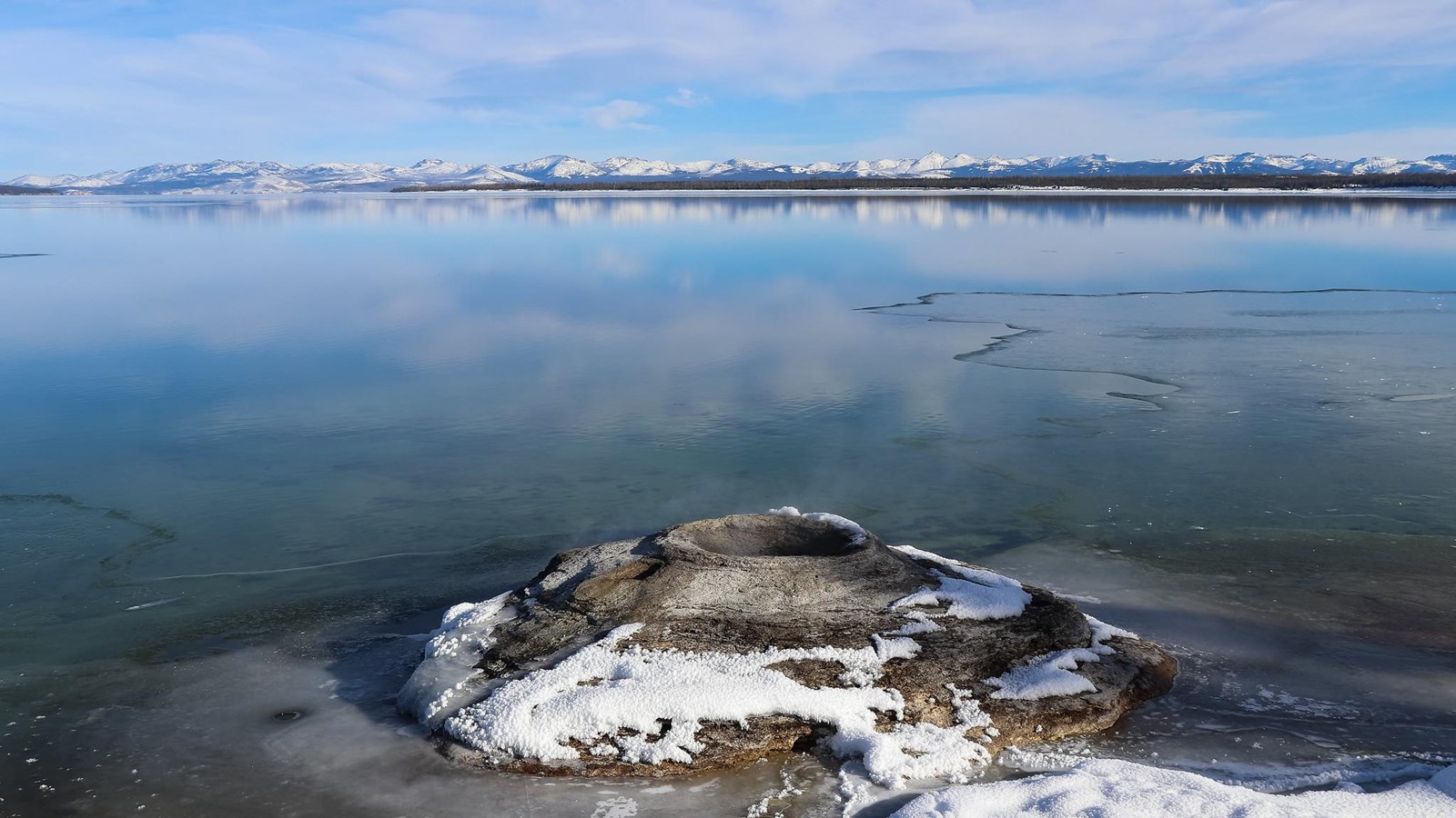 A geyser cone emerges from the water in a large lake.
