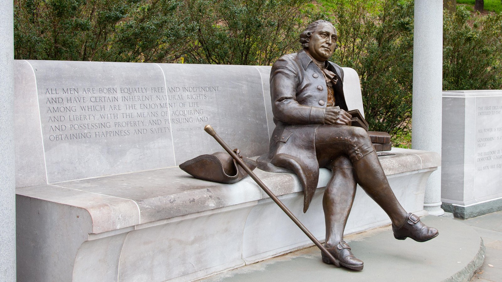 Bronze statue of a reclining man in Colonial dress on a stone bench
