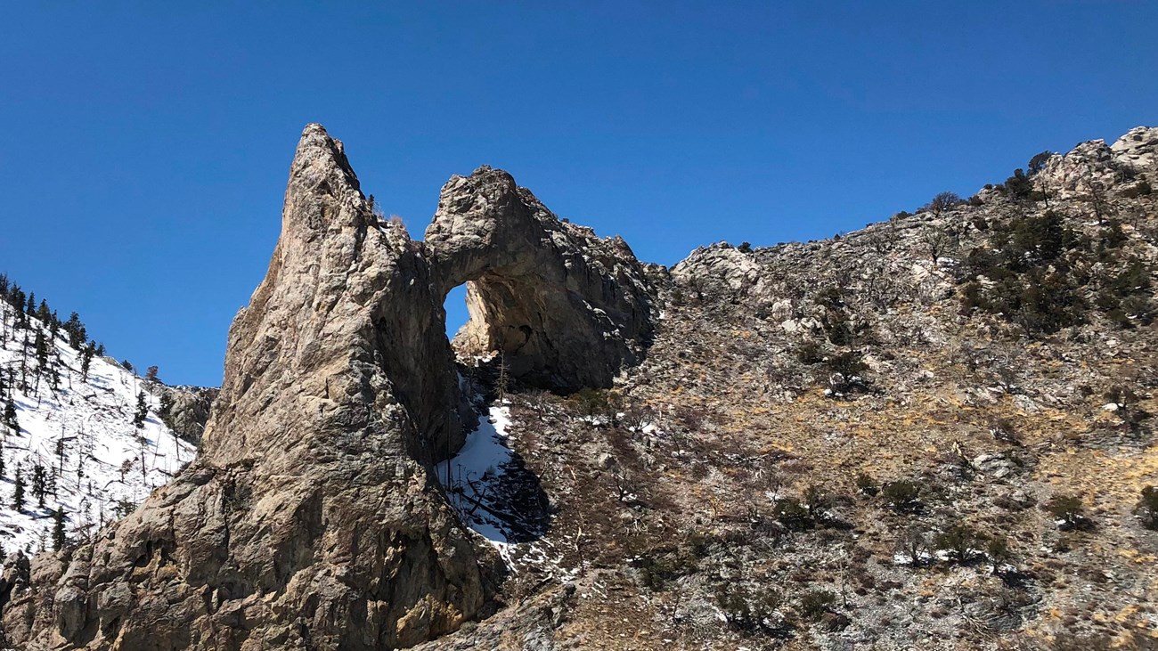 Large tan limestone arch with snow on the ground.