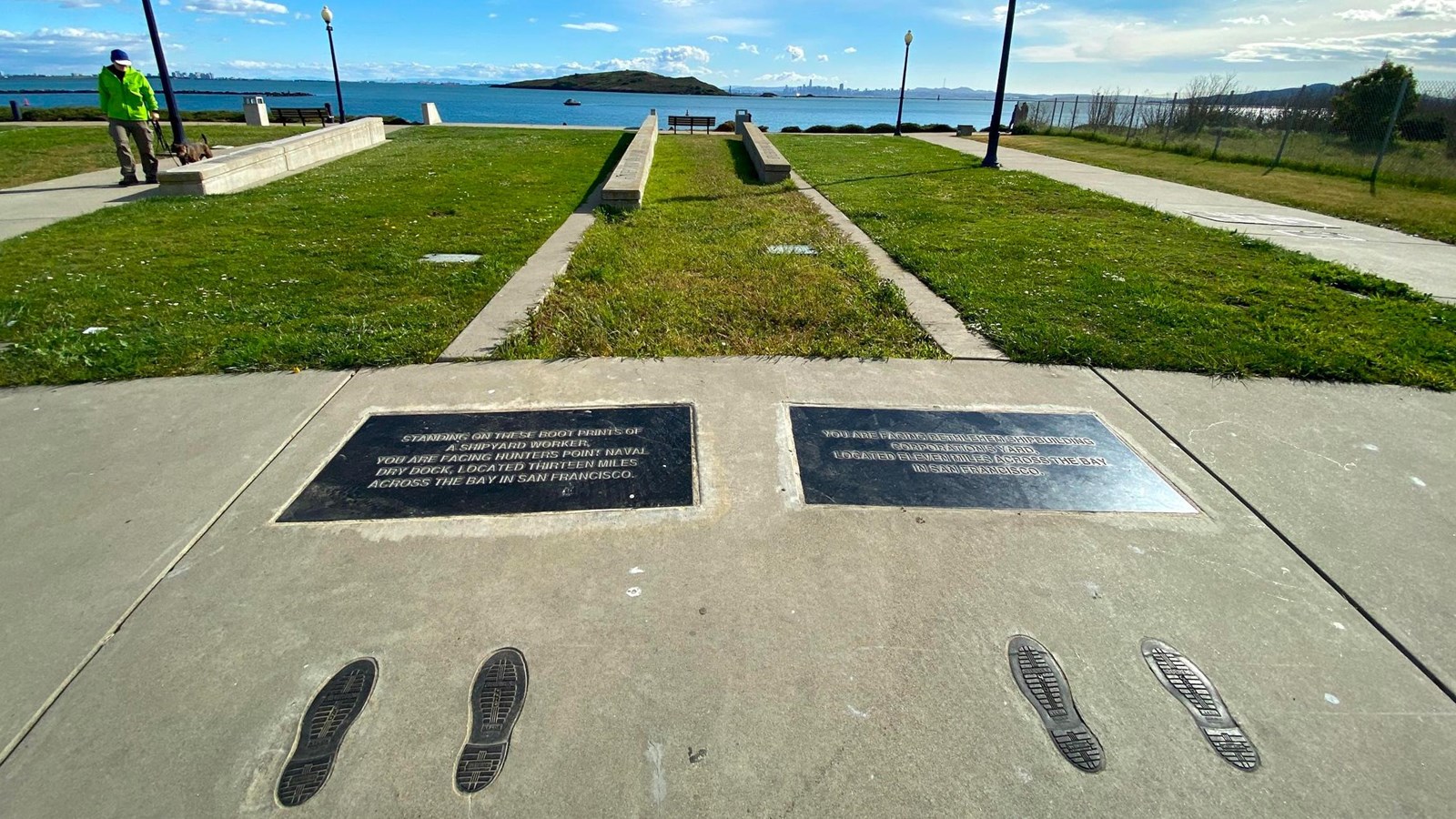 Two bronze plates a two pairs of bronze feet prints are embedded in concrete. Ocean, grass are seen.