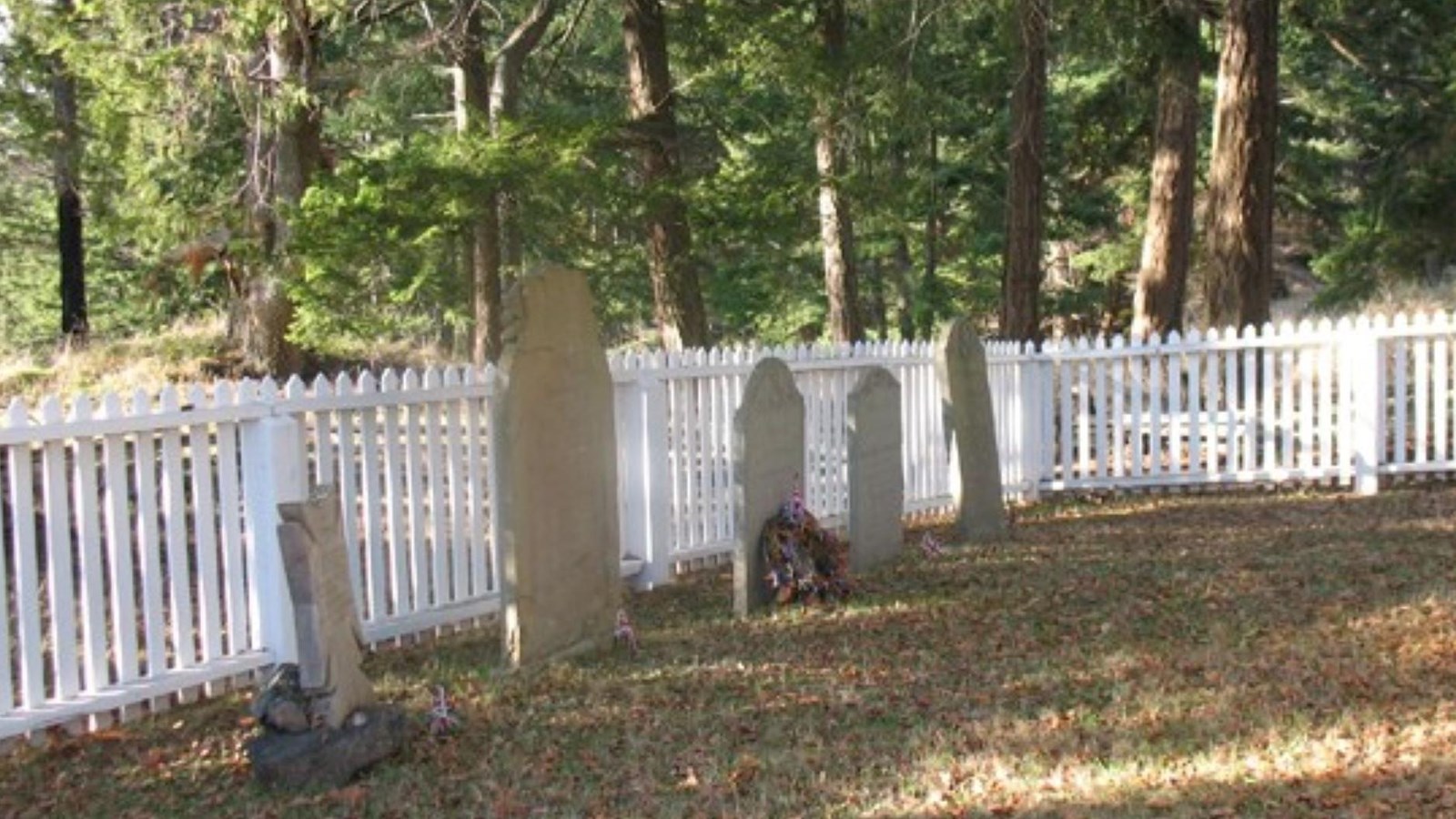 Color photograph of headstones in front of a white picket fence