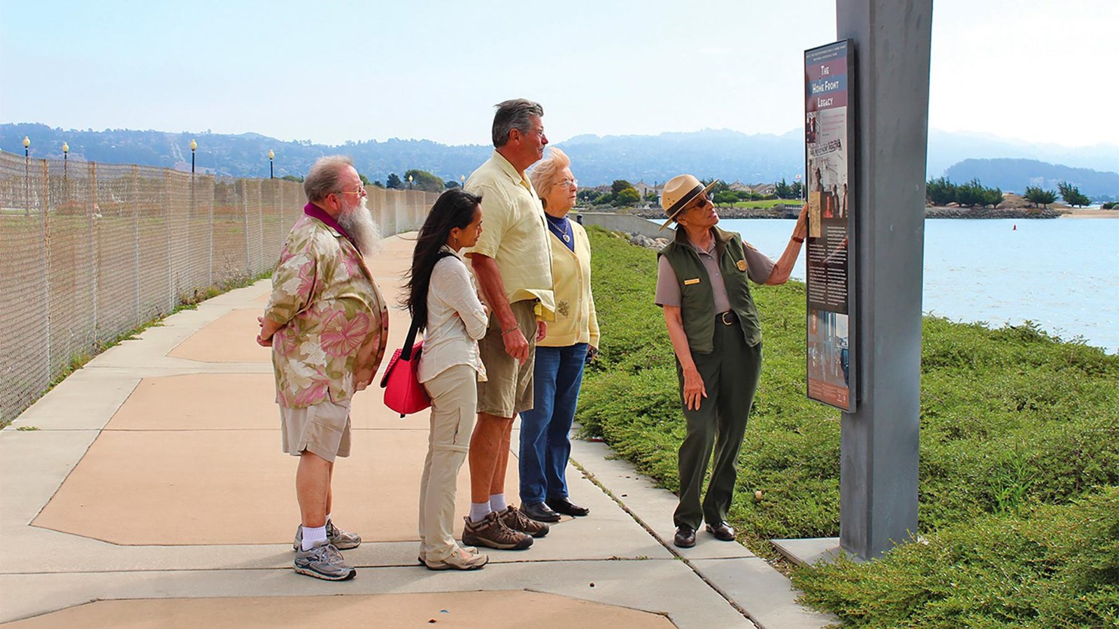 A female  ranger, two other women and two men view a wayside marker on the Bay Trail.
