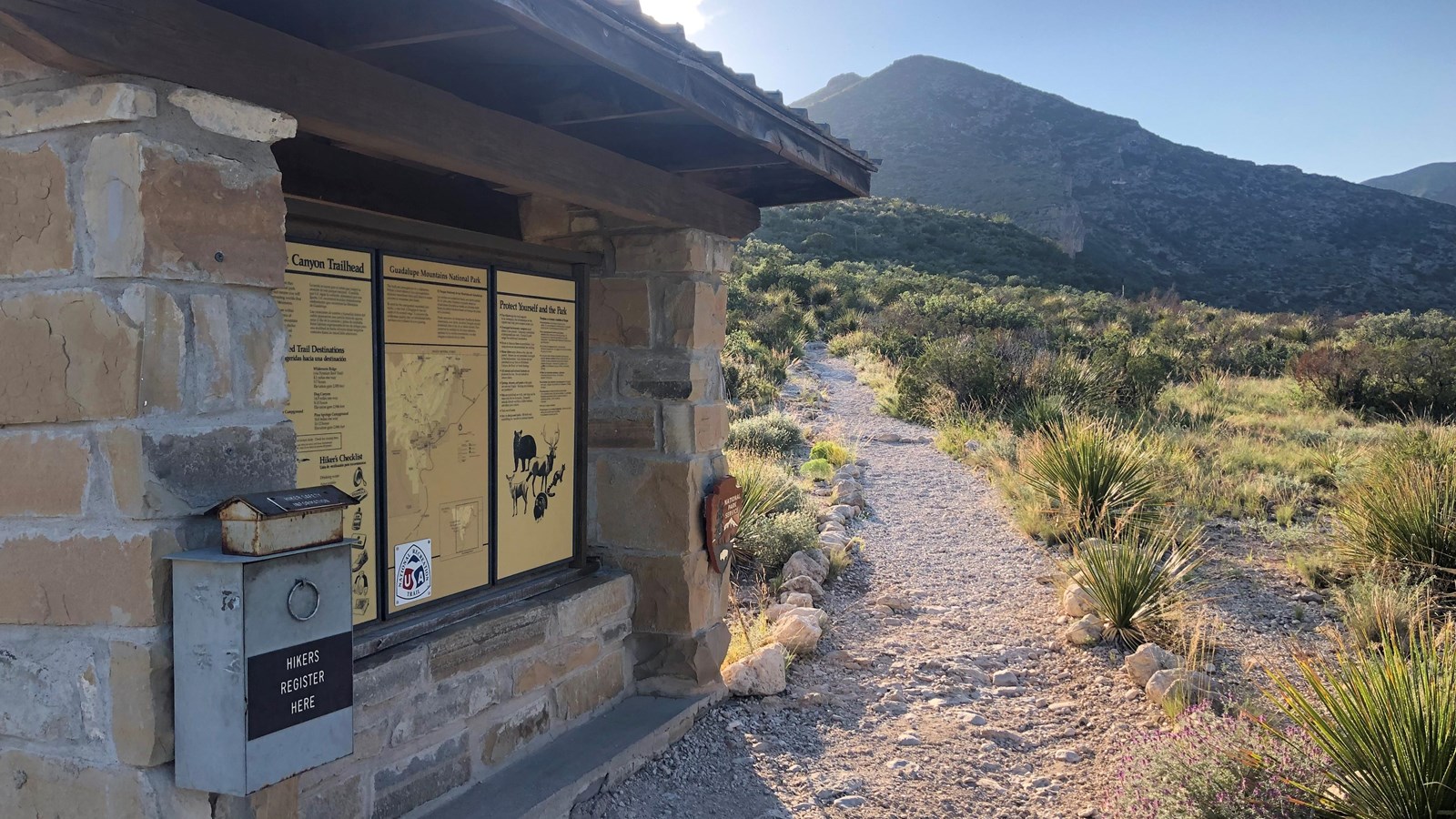 A stone kiosk with trail information in a desert mountain landscape