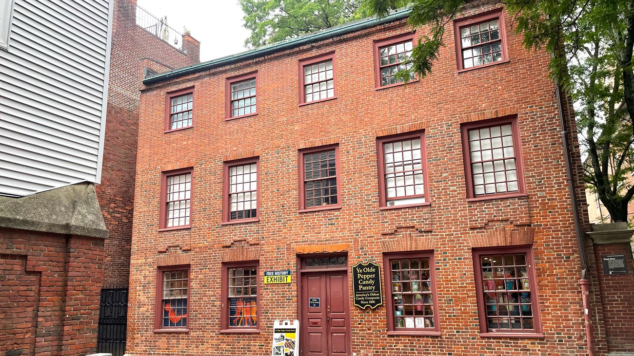 a three-story brick building. There is a central reddish-brown french door and paned windows.