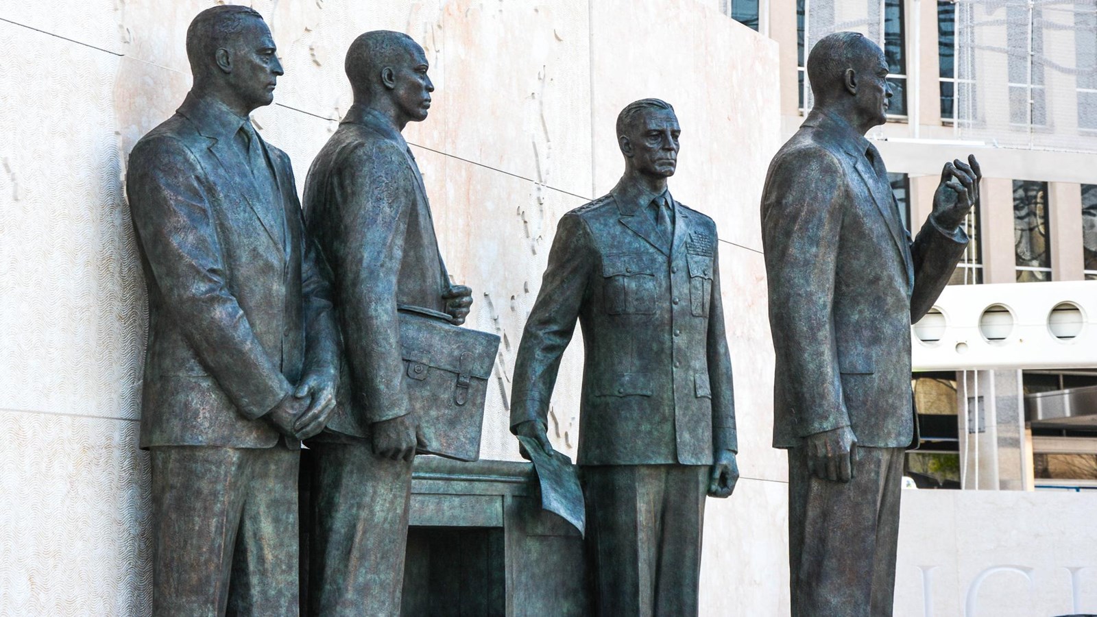 4 bronze statues standing in front of a desk with a map in the background.