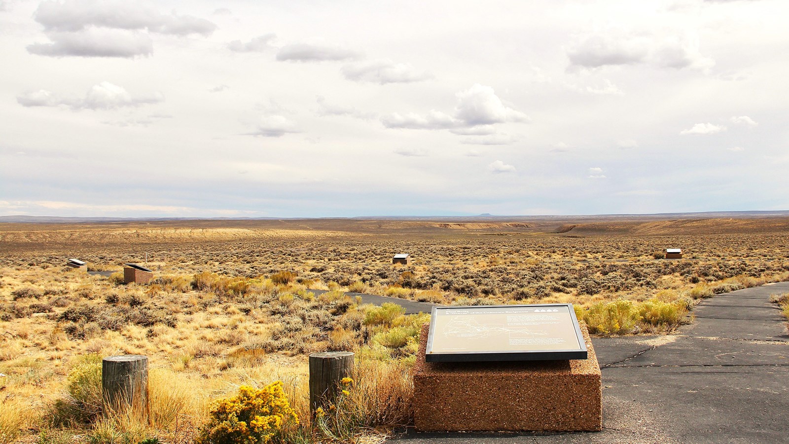 A blacktop path and wayside exhibit sit at the lower right corner of the image with grass around.
