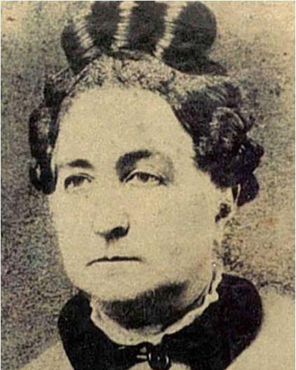 A middle aged woman with her hair in a bun and a button up jacket with a black color.