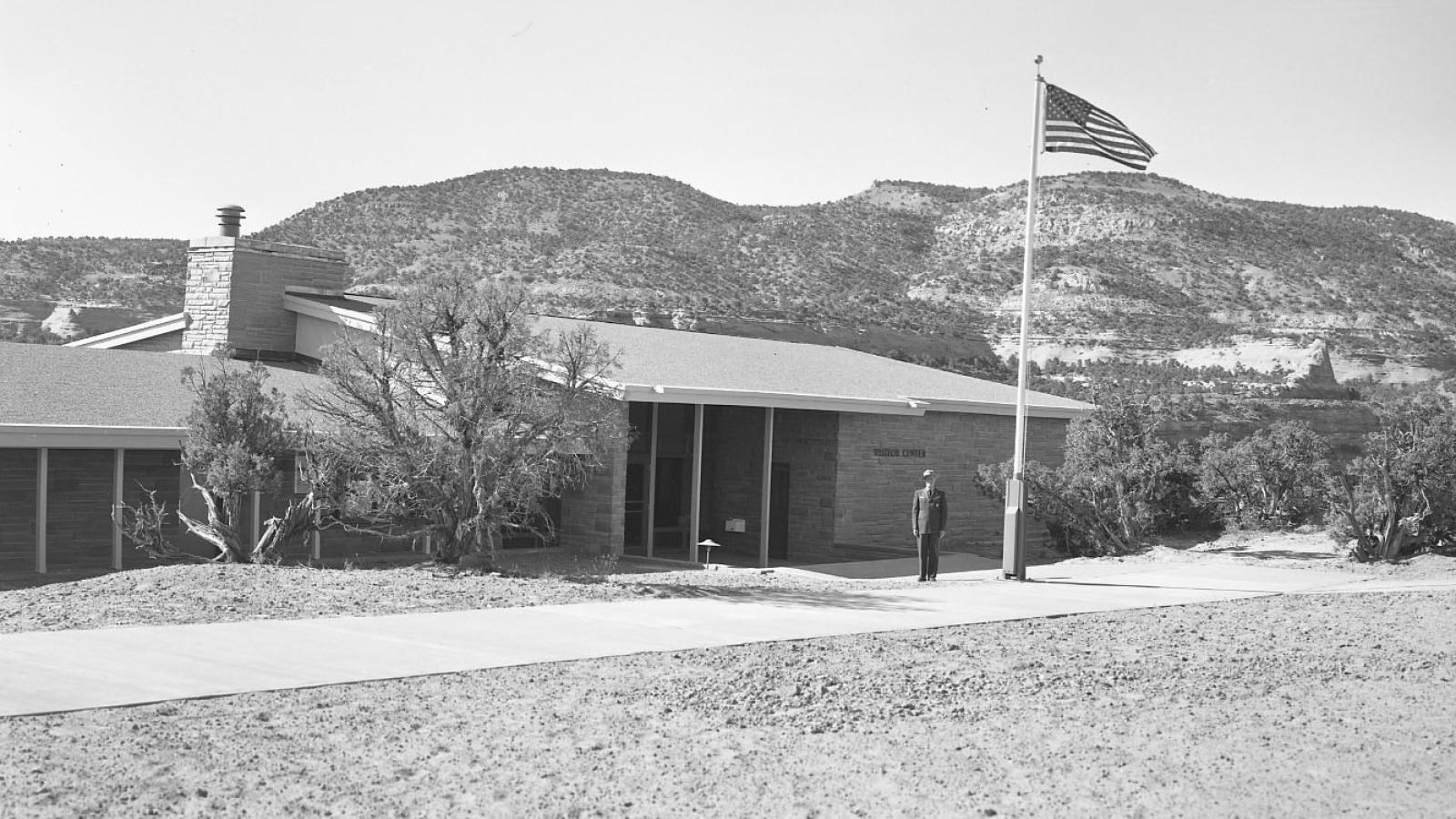 Black and White image of typical 1960\'s building with low almost flat roof and man in uniform.  