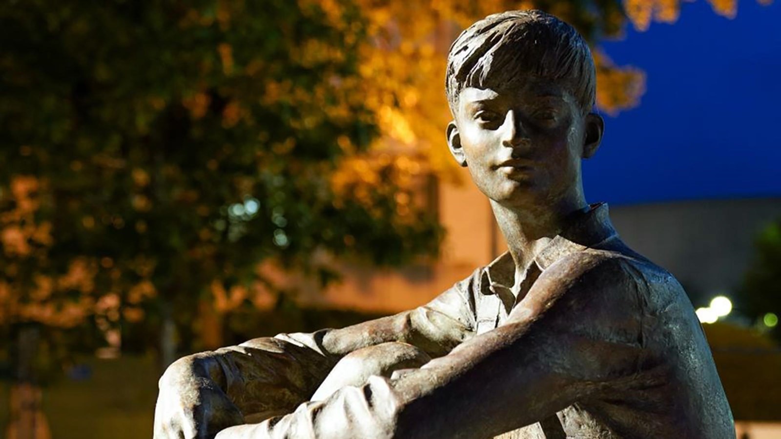 A bronze statue of a young boy sitting on a pedestal.
