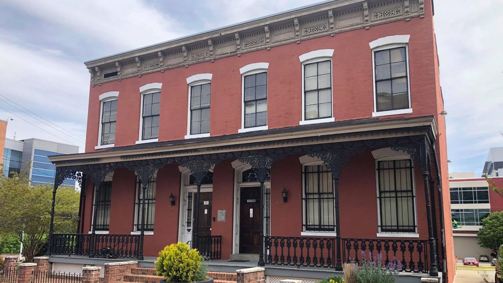 two-story red brick duplex building, porch with black metal fence surrounding the porch.