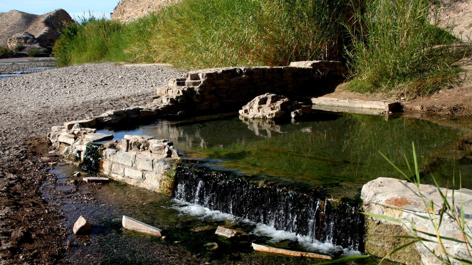 A pool of fresh water pours out of the ruined foundation of a desert hot spring bath house.