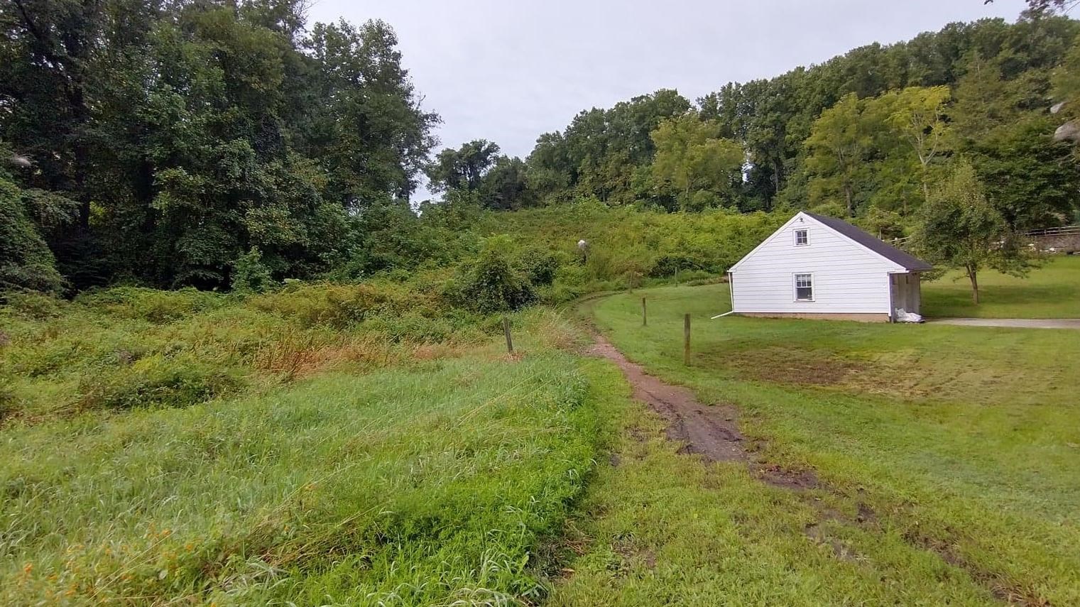 A dirt trail surrounded by green flora wraps behind an 18th century home. 