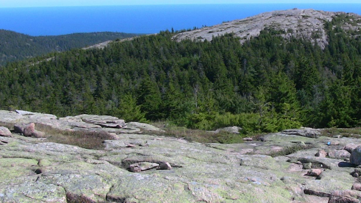 a view from a rocky summit looking out to another rocky summit, ocean, and blue sky