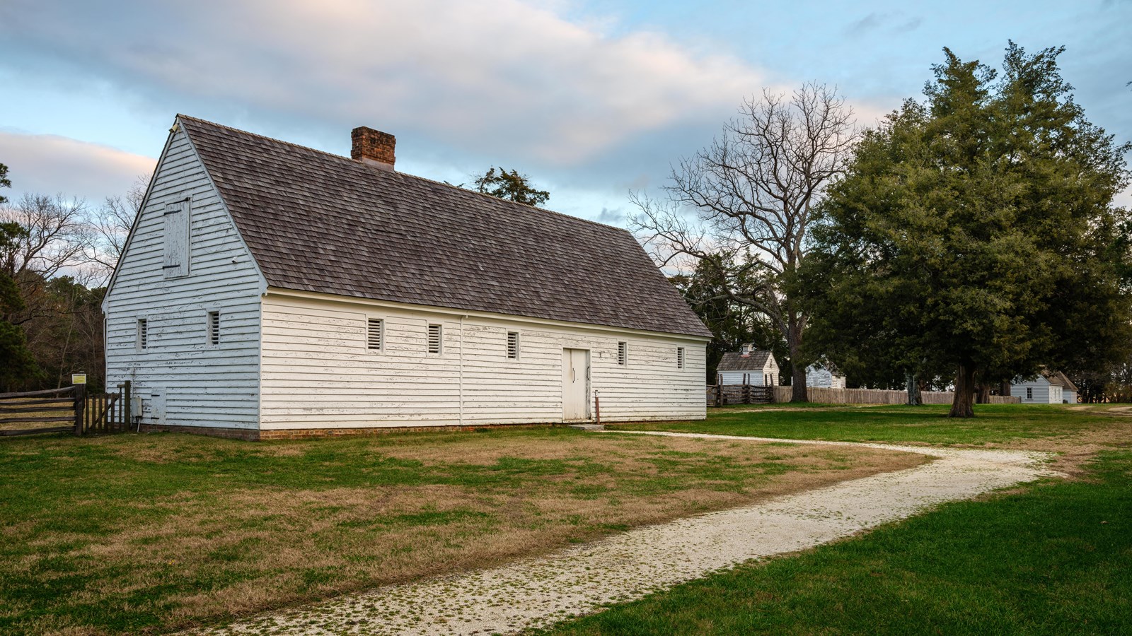 A white barn sitting in a field surrounded by trees with a gravel path leading to the door.