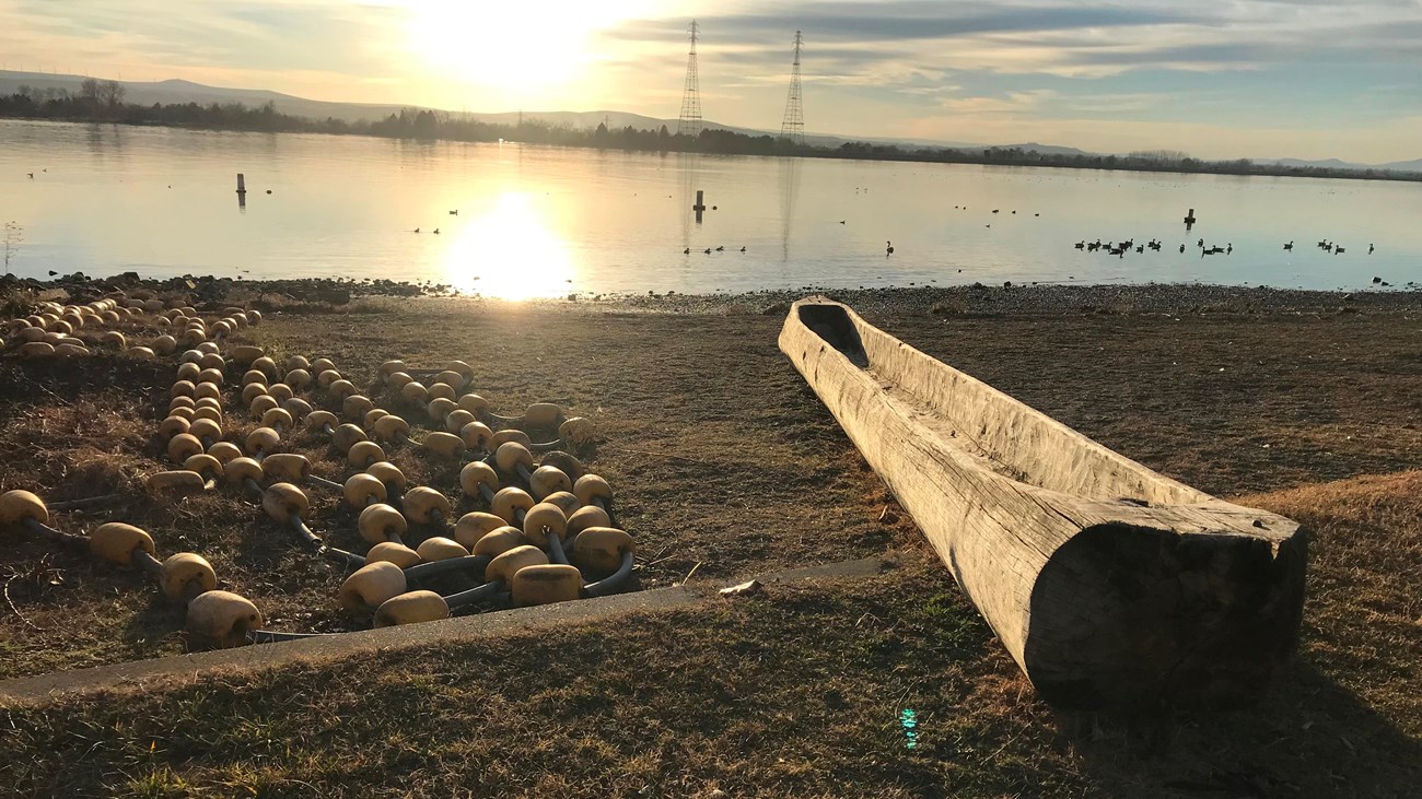 A color photo  of a large body of water with distant shores. There is a log dugout into a canoe.