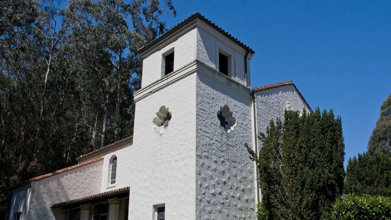 A view of the stucco tower with a red Spanish tile roof on the corner of the chapel.