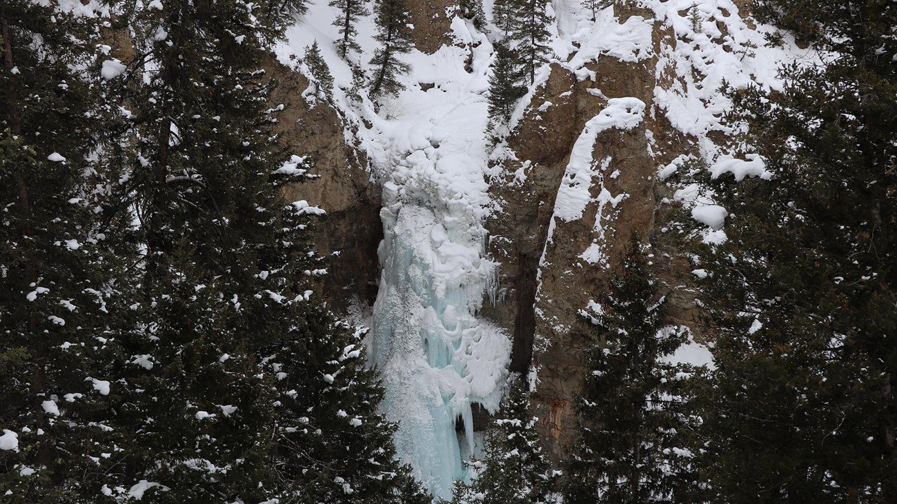Icicle formations encase a waterfall surrounded by columns of rock.