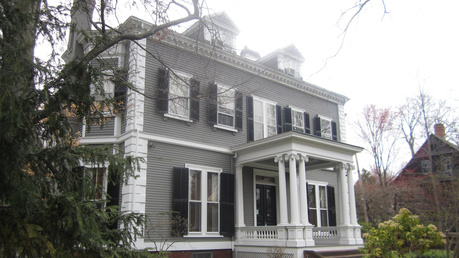 Two story grey house with white trim, protruding porch, and two dormers.