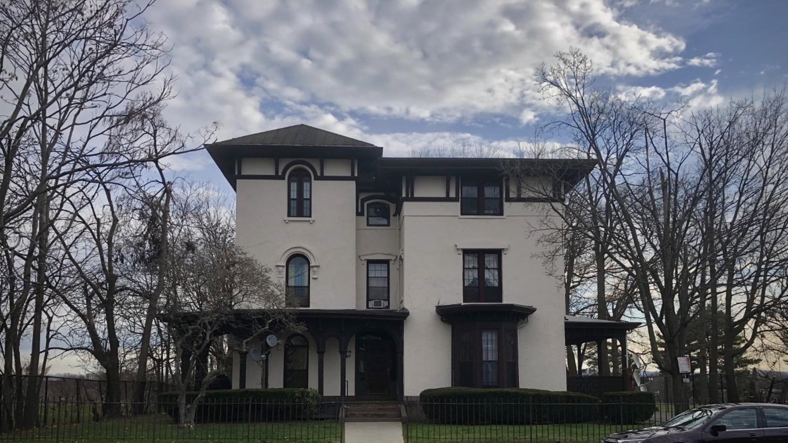 A cream stucco Italianate House with brown trim and a porch on a cloudy fall day. 