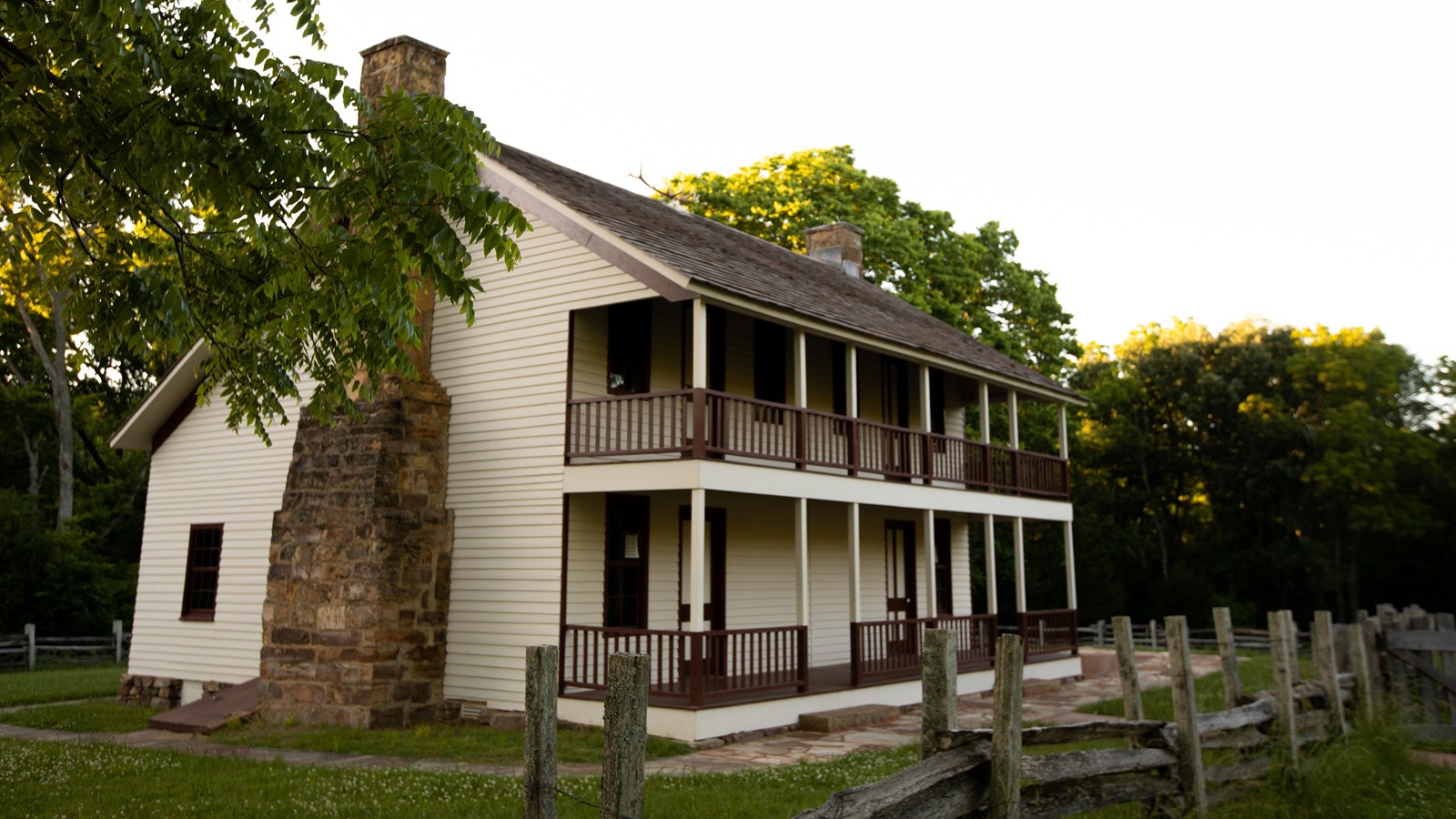 Photo of a cream color two story farmhouse, with maroon trim and sandstone chimneys.