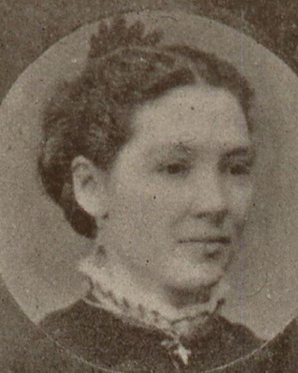 An image of a woman with her hair up in a dark shirt with a white collar.