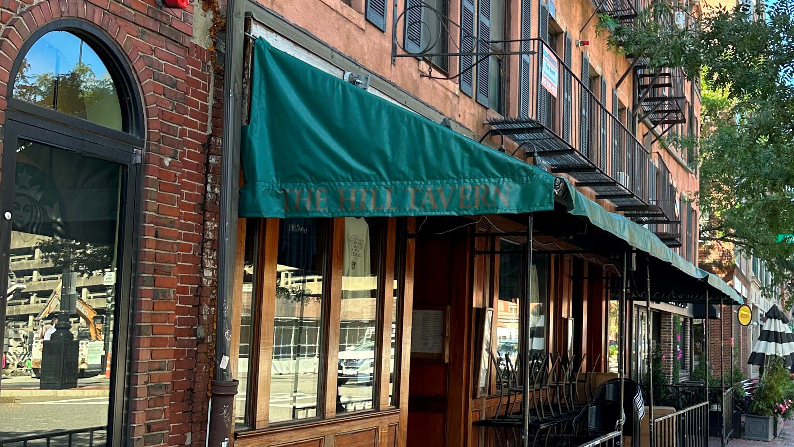 Photo of a brick building with a green awing over an outdoor patio with a small metal fence