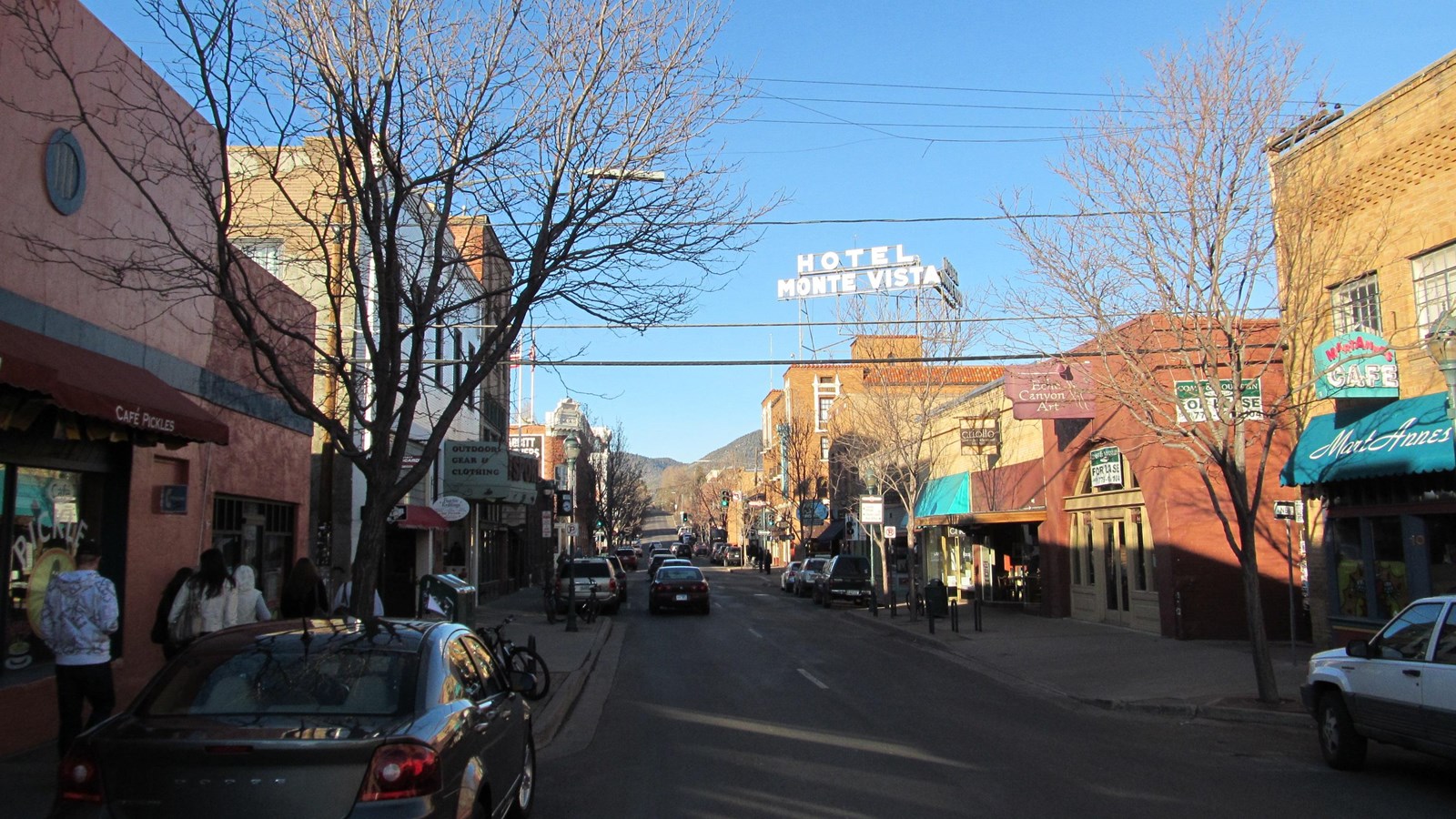 A town street with red brick buildings with cars parked along the sidewalks.