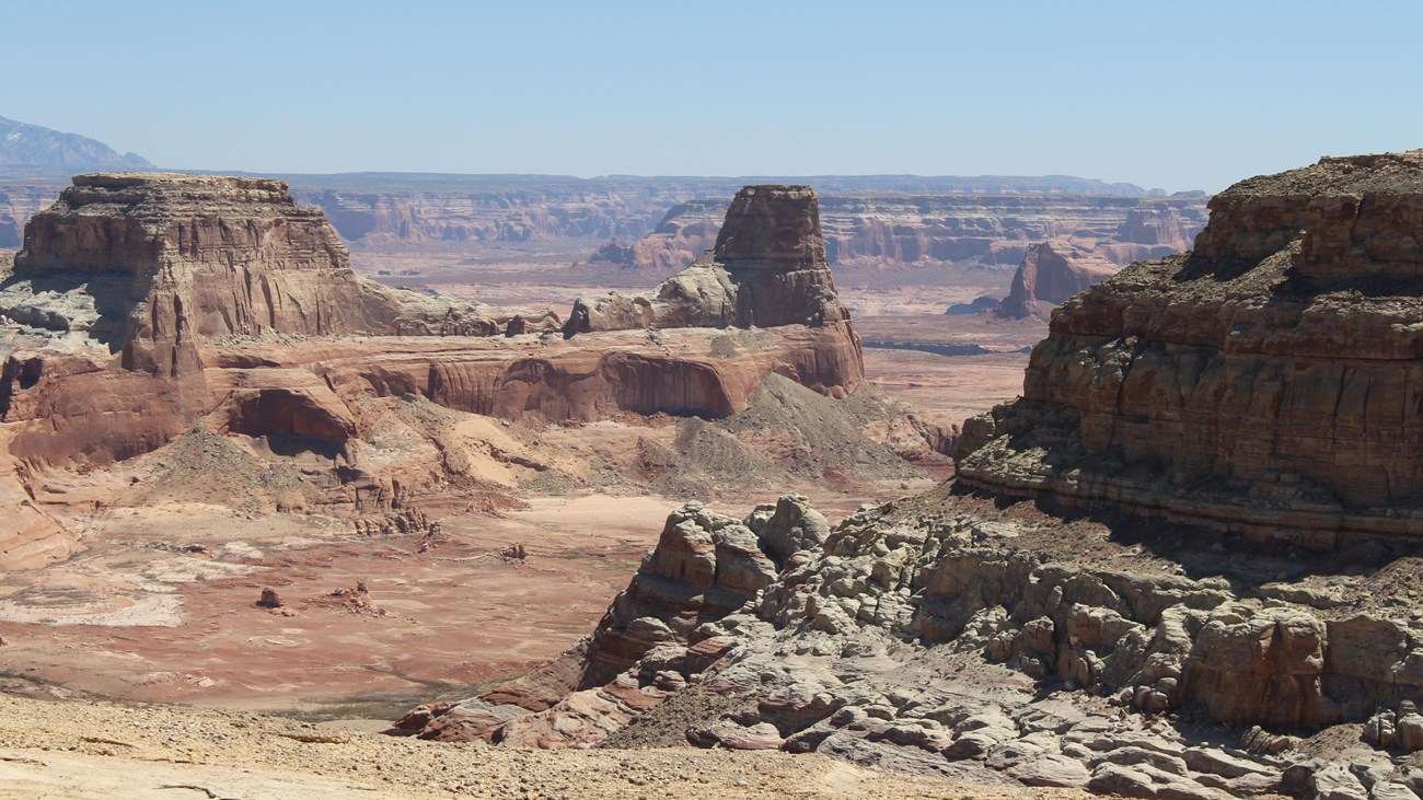 Sandstone cliffs, buttes, and mesas. Just a bit of a lake in the distance.