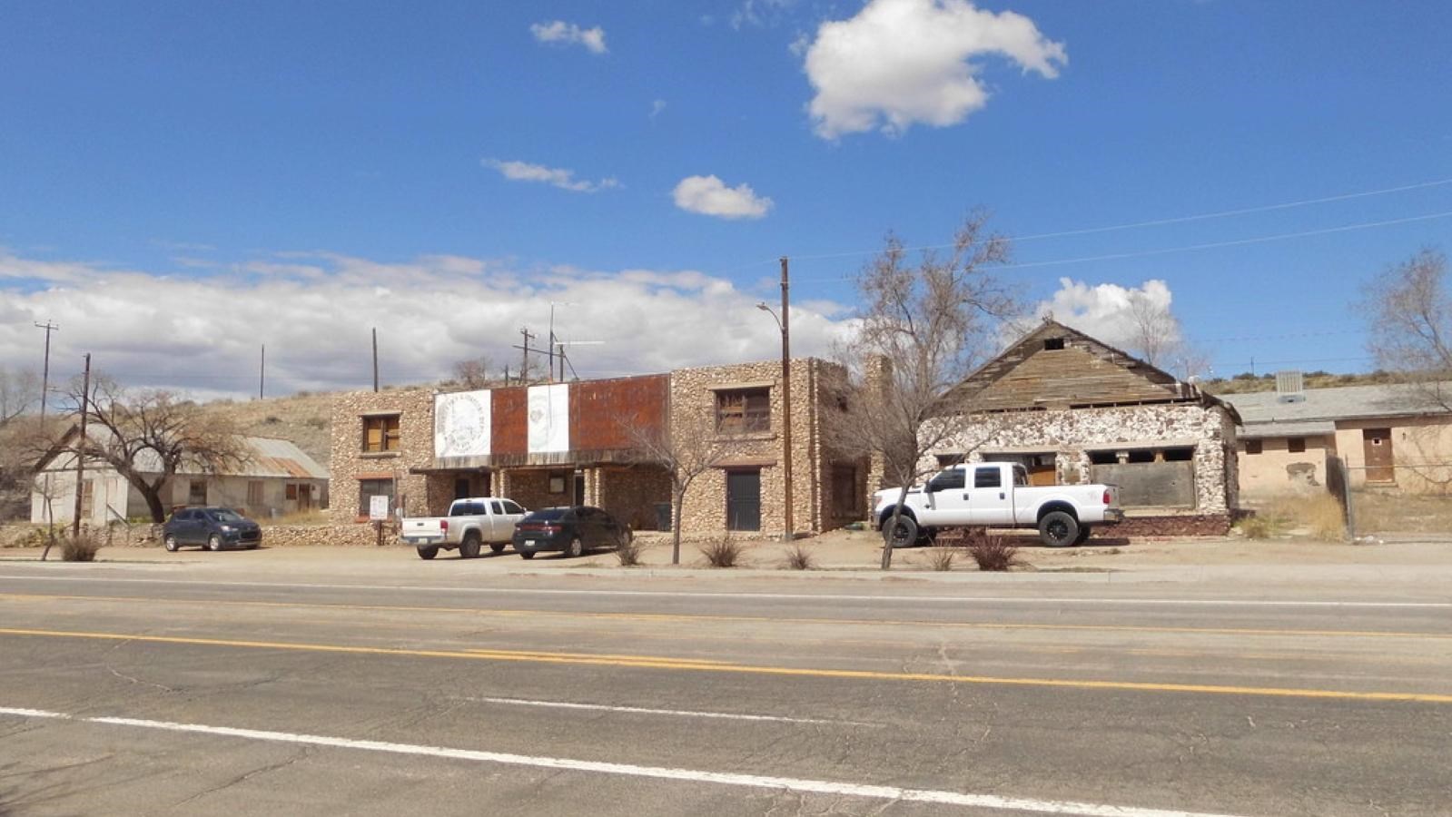 Two red brick buildings, one with a flat roof, the other with a peak sit along a road.