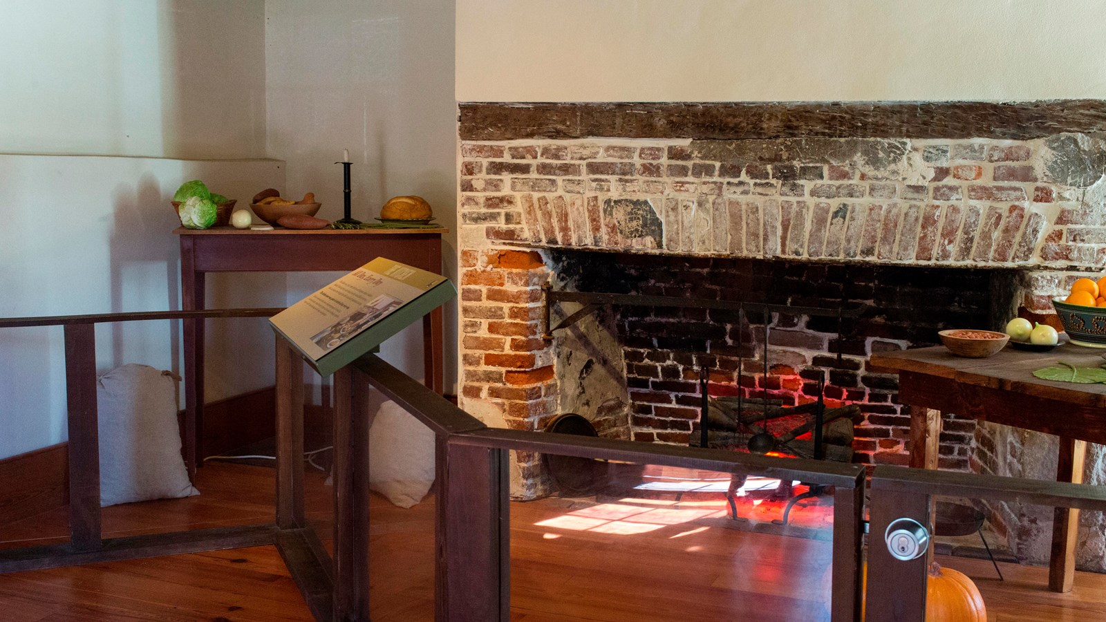 an exhibit wall in front of two tables covered in fake food, and a wide brick fireplace