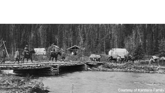 a log bridge over a creek leading to wall tents and tethered horses