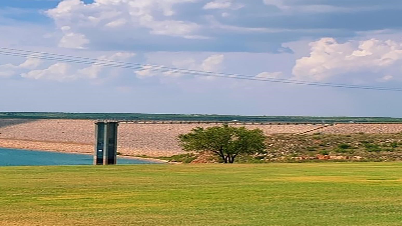 A view of Sanford Dam and Lake Meredith.  The sky is blue with clouds. 
