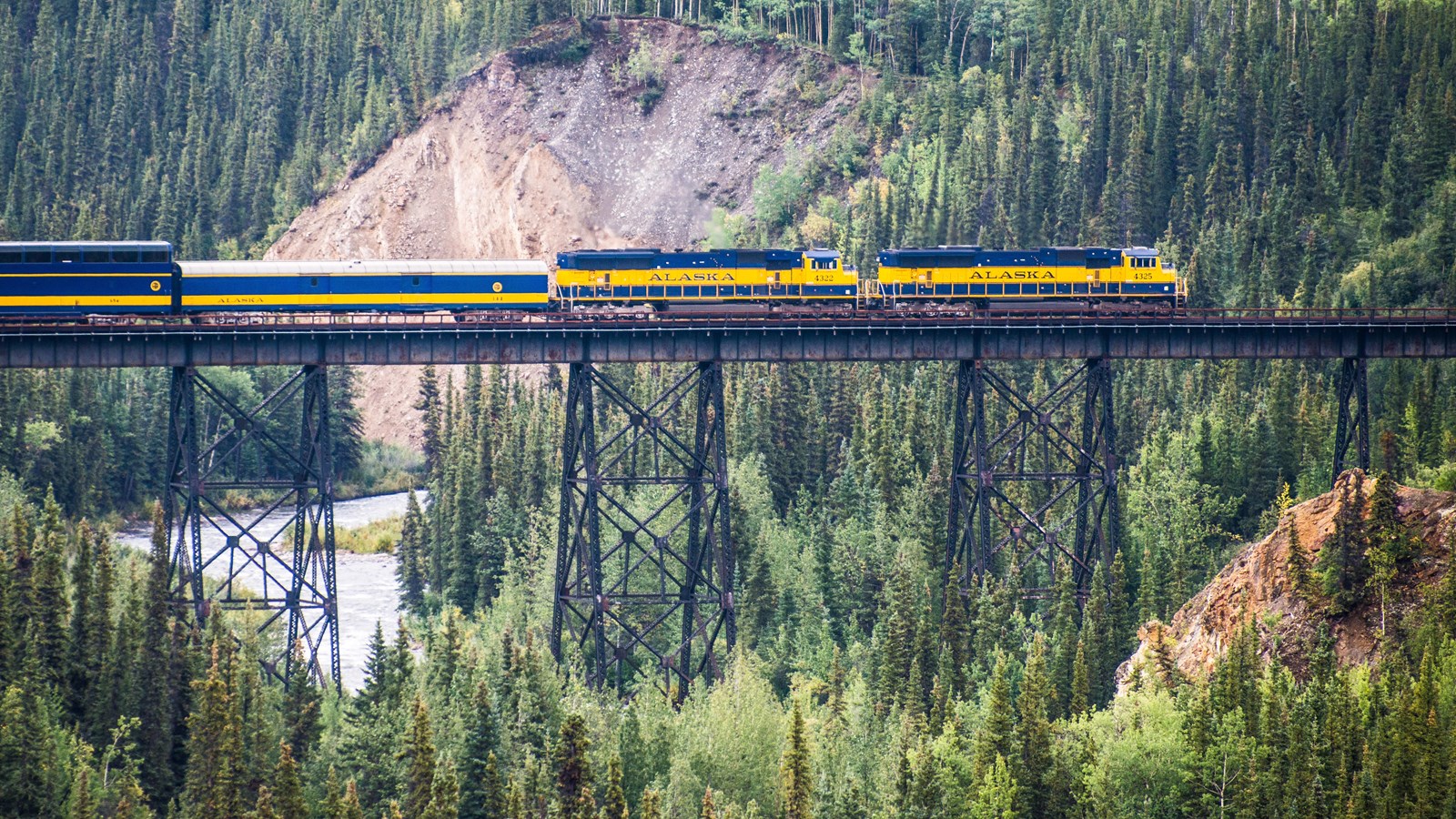 a train on a bridge spanning a deep gorge over a shallow creek