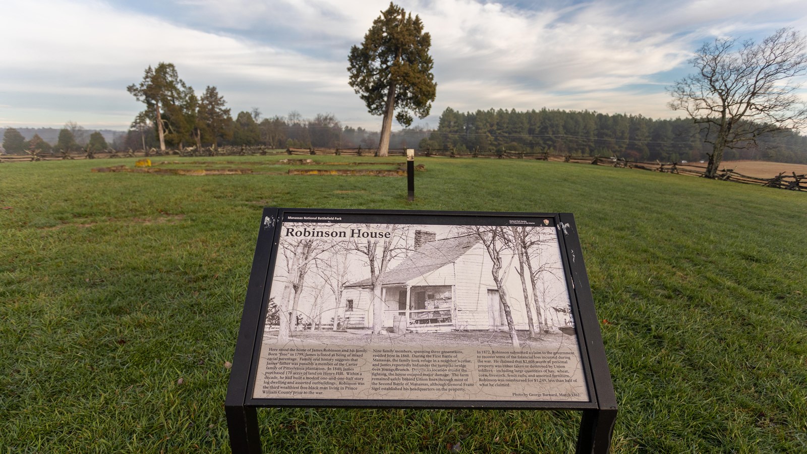 An informational panel in front of a grassy field. 