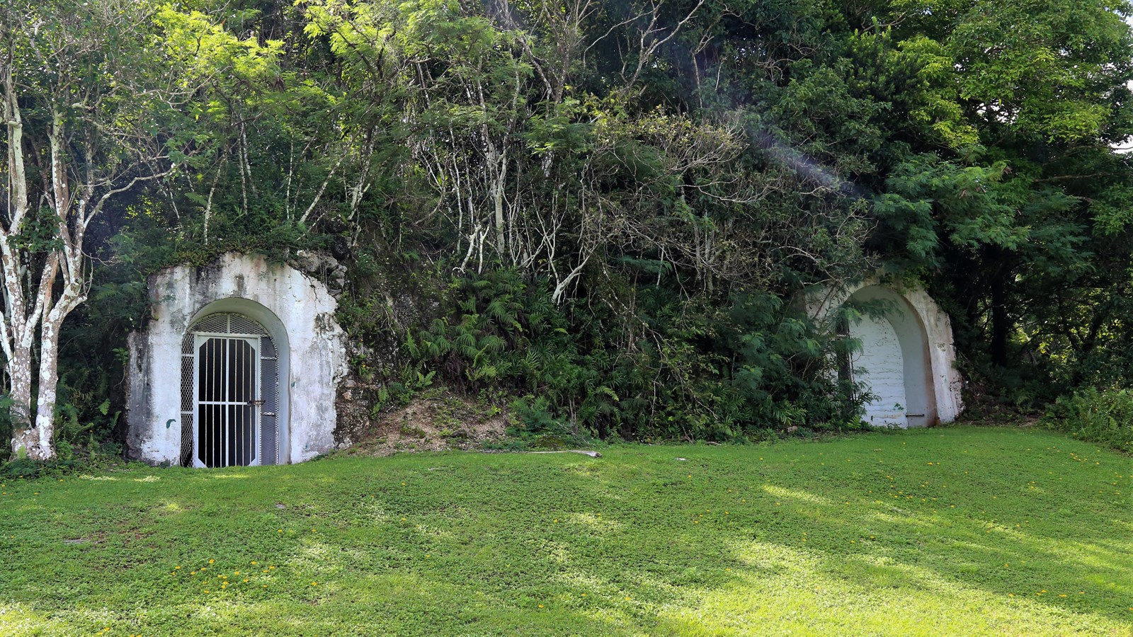 Two gated concrete arches set into a hill covered in greenery.