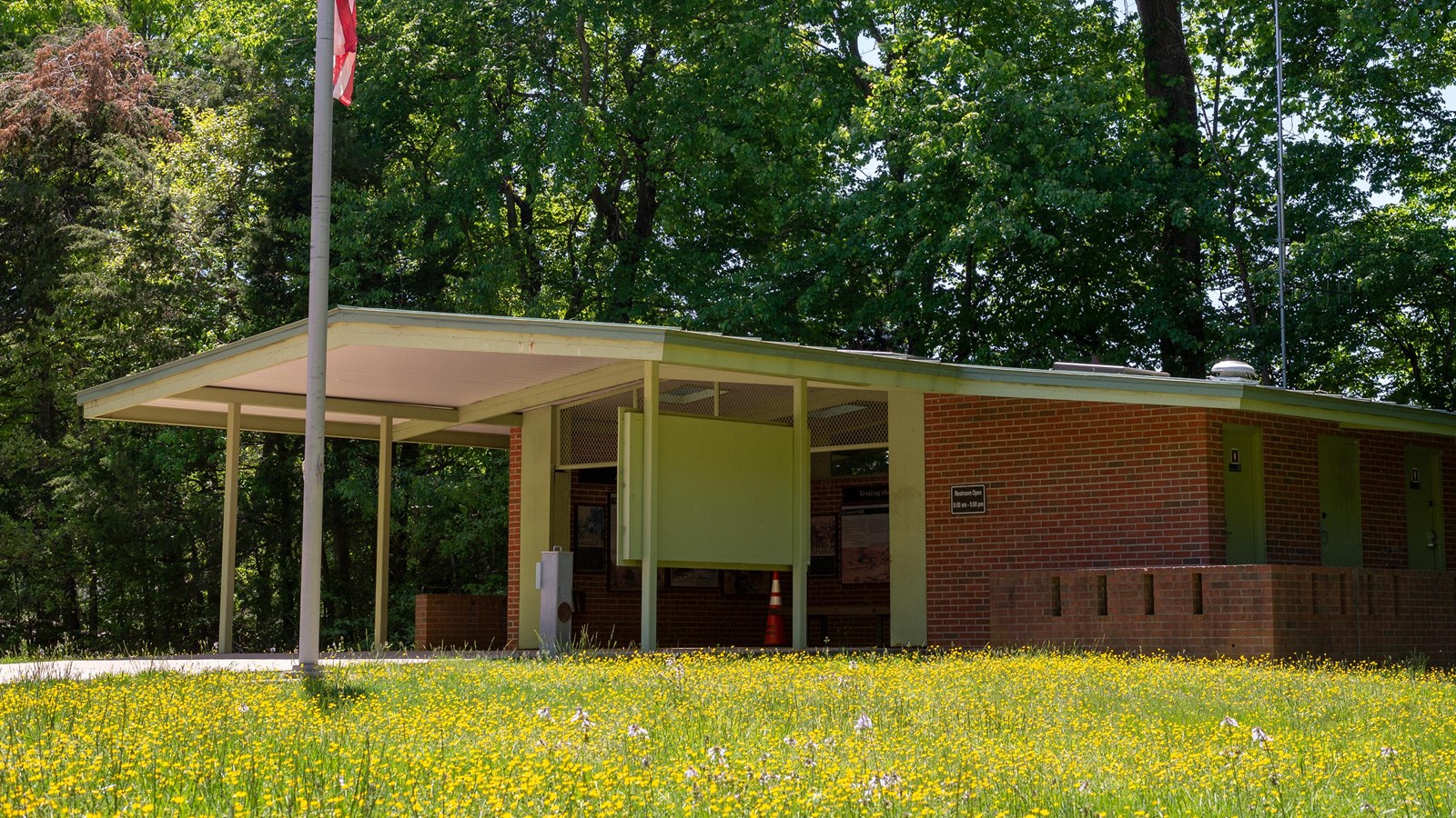 A single story sheltered enclosure with interpretive panels and a flag outside.