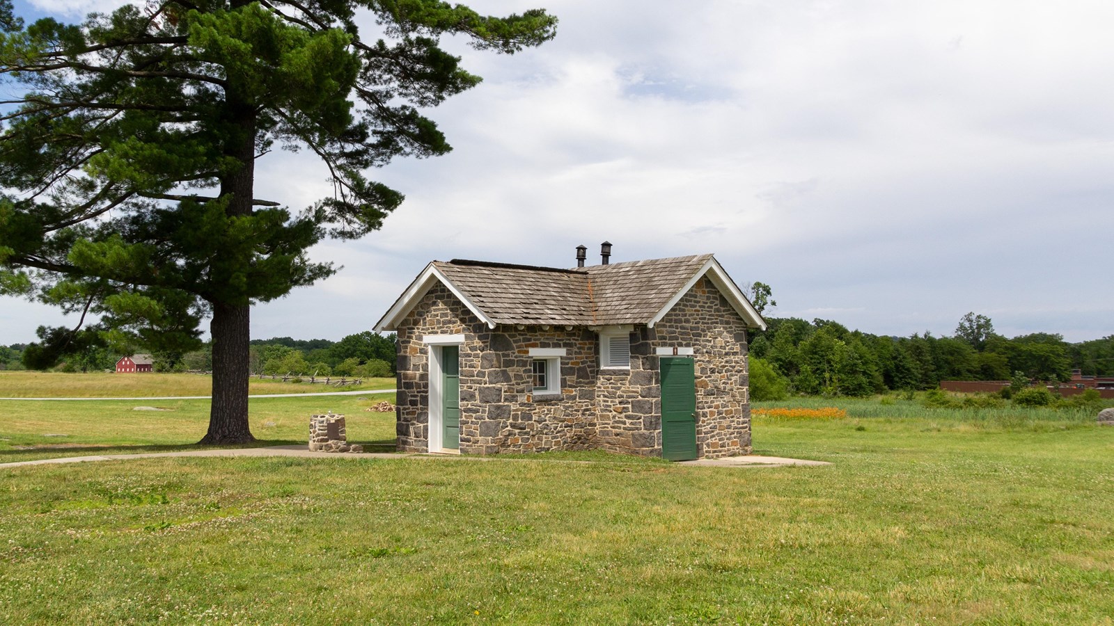 A single story stone structure in a field with a-frame roof and two doors on opposite walls.