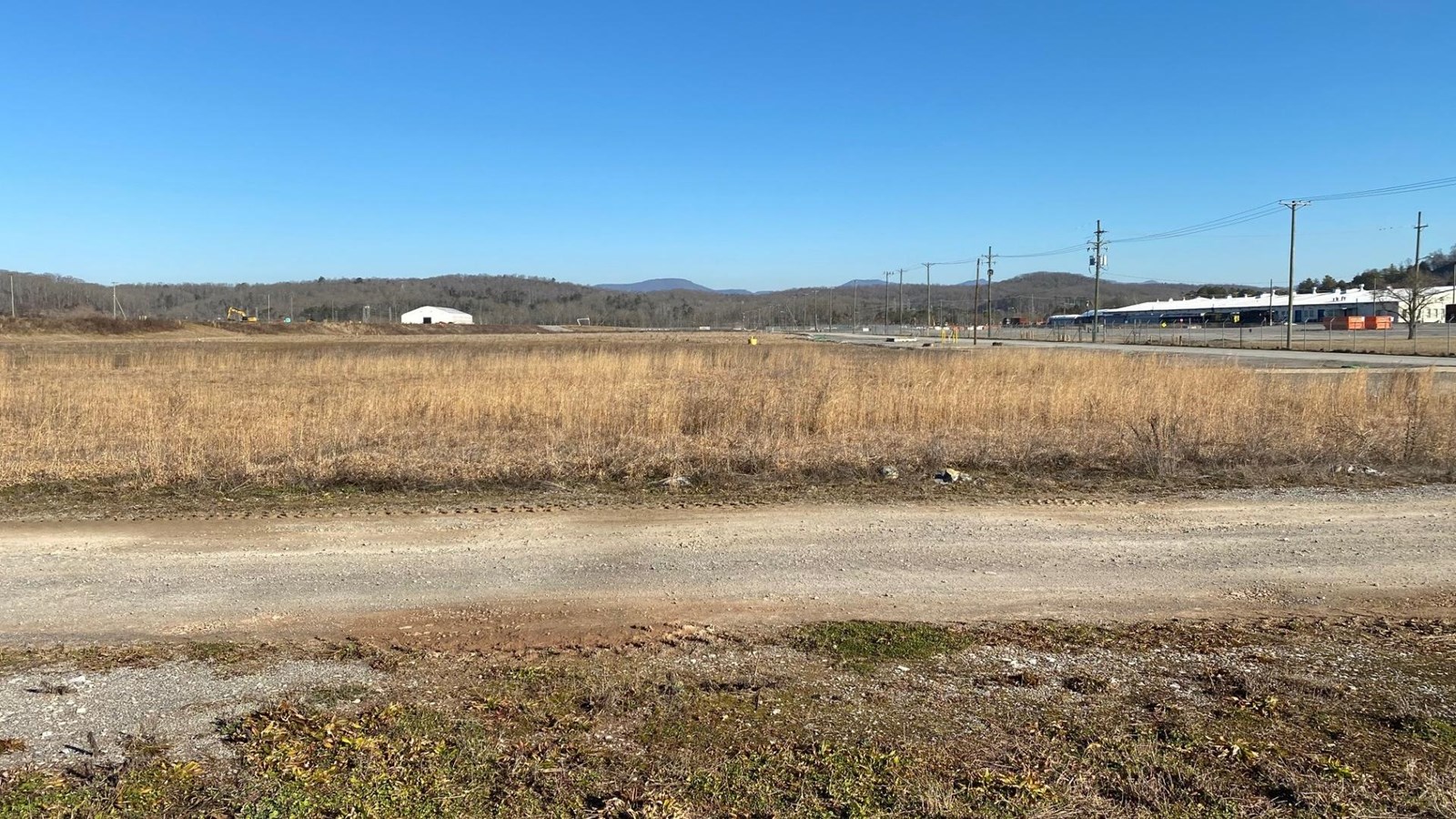 An expansive grassy field with a large building in the distance and a ridgeline in the far distance.
