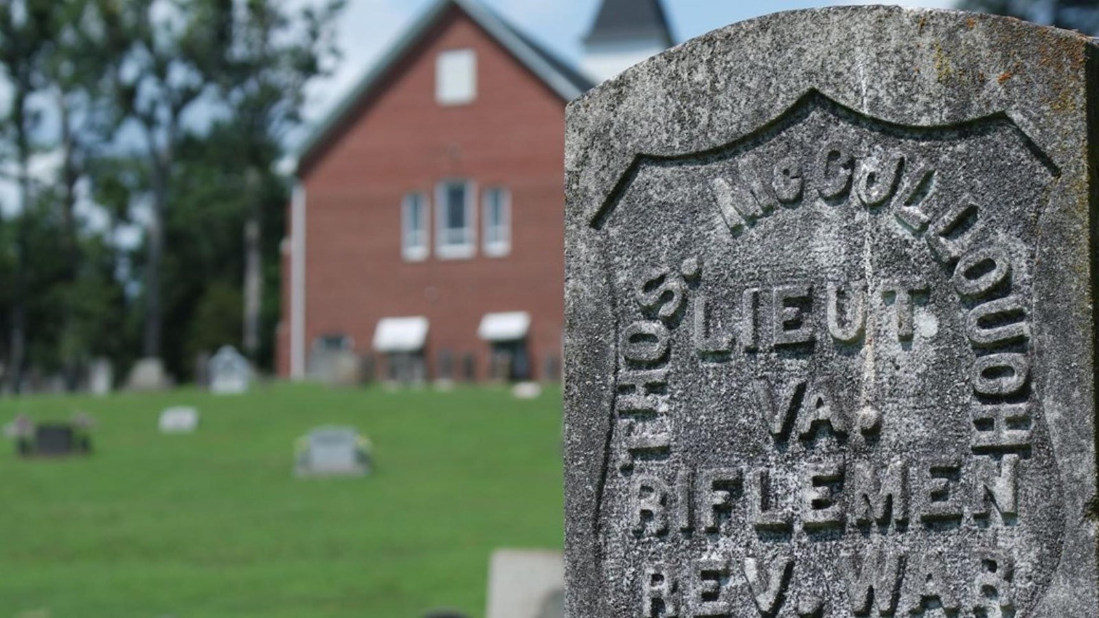 A gravestone is in focus with a blurred church and graveyard behind it.