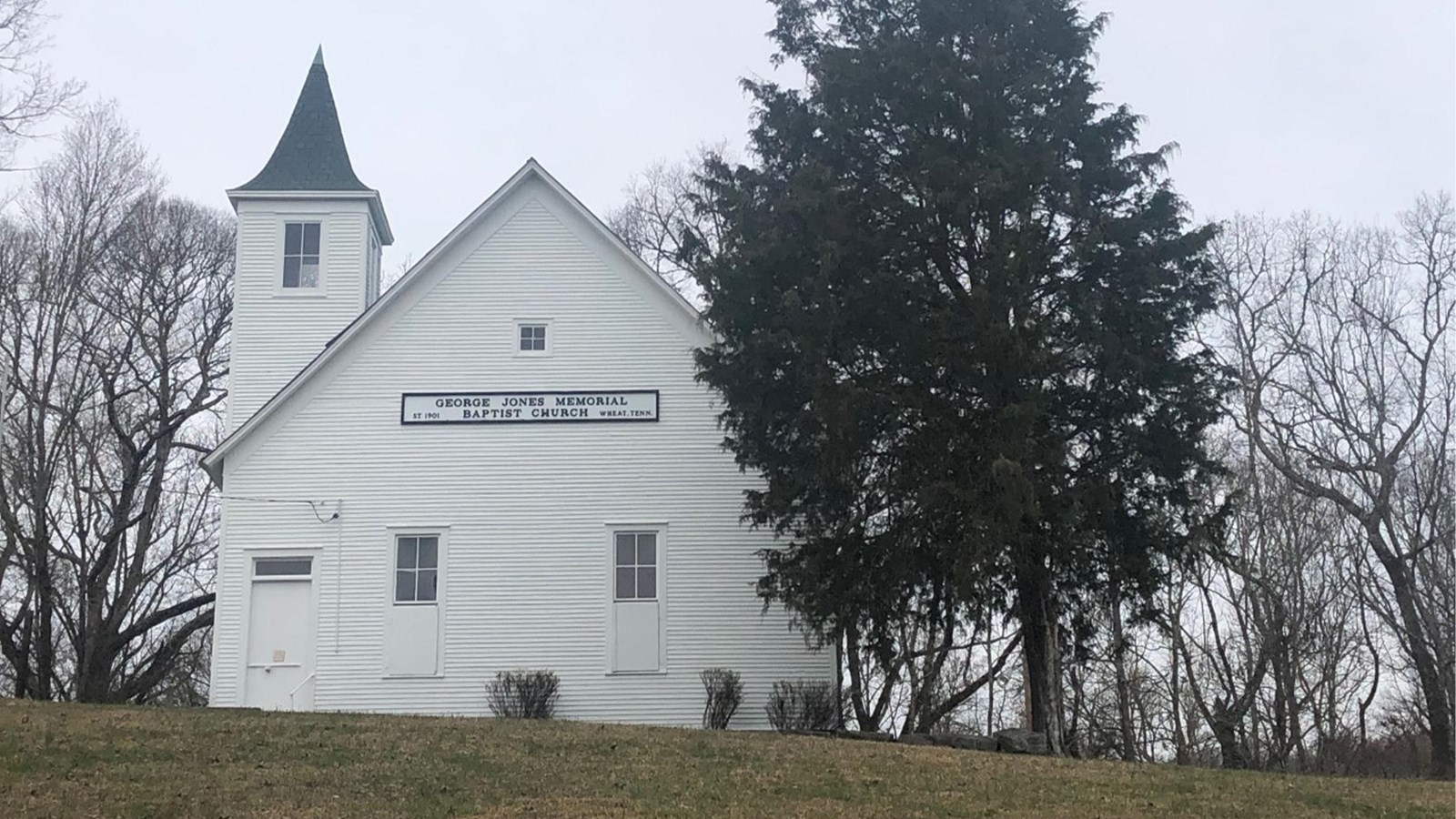 Large white church with tall steeple on wooded hill