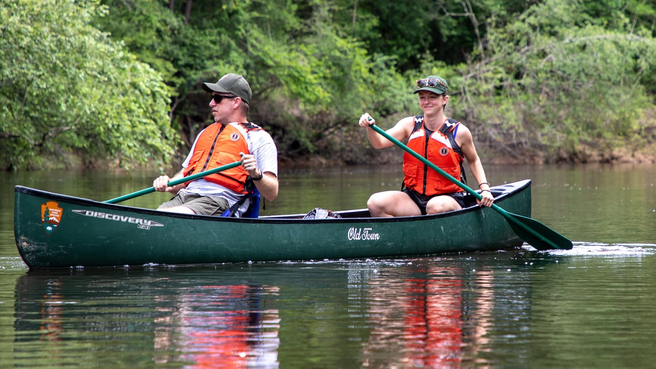 2 people paddling a green canoe on a creek