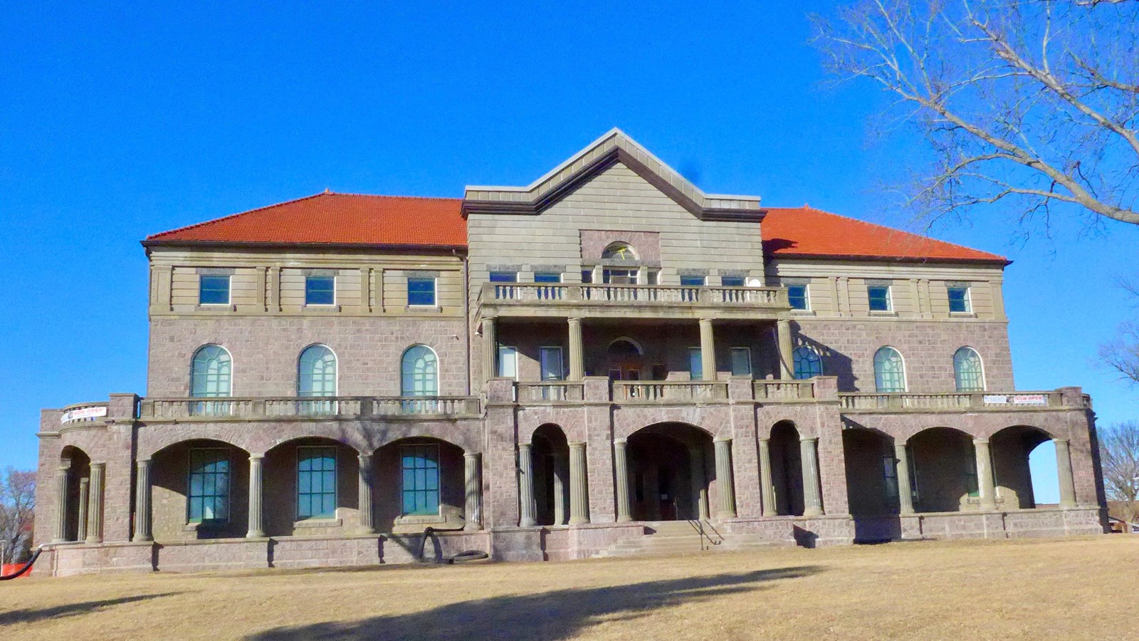 Three story brick building with columns and a red roof